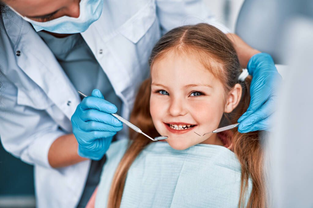 Фотографія дитини, яка посміхається за призначенням стоматолога. Лікар в рукавичках тримає інструменти для обстеження. Дитяча стоматологія.                                - Фото, зображення