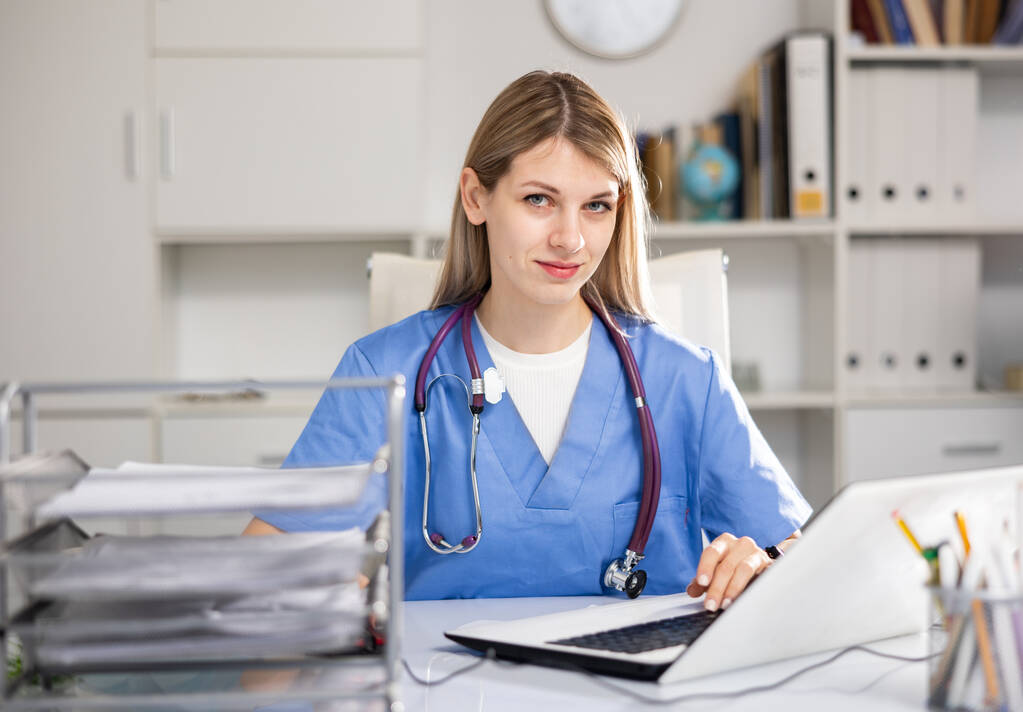 Young woman doctor sitting at table in her office and looking at camera. - Foto, Imagen