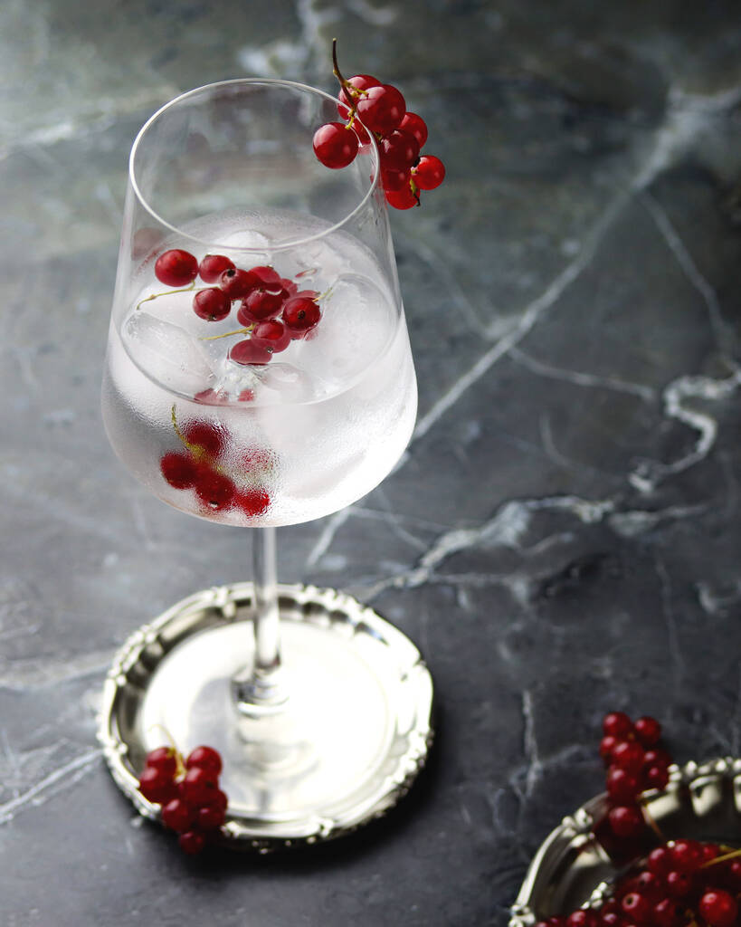 Widok z góry na mrożoną wodę z czerwonej porzeczki. Świeży koktajl owocowy na zimno w kieliszku do wina, orzeźwiający letni napój jagodowy z porzeczki na kamiennym betonowym tle - Zdjęcie, obraz