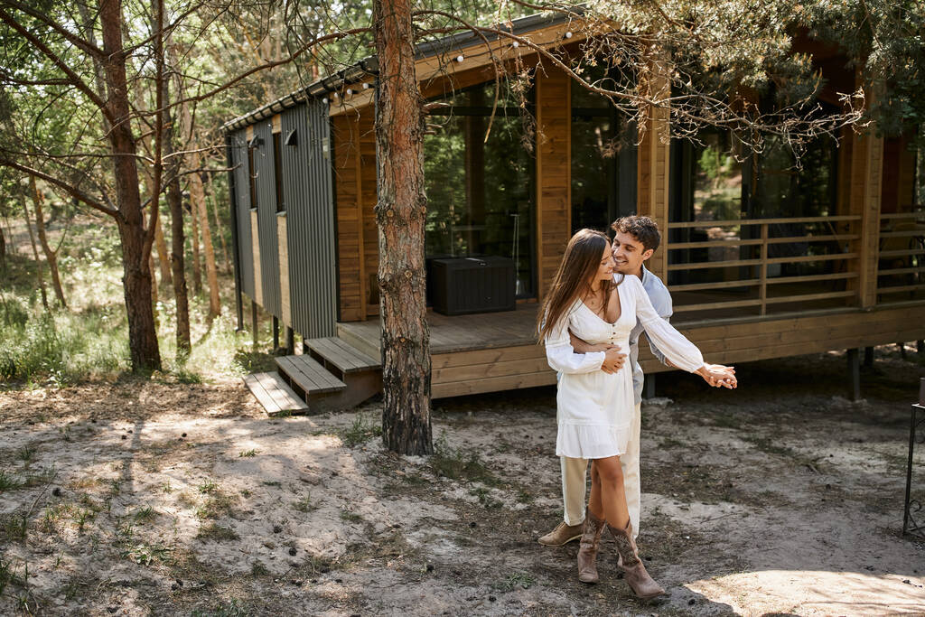 felicidade e riso, homem abraçando mulher perto de casa de férias, na floresta, verão e romance - Foto, Imagem