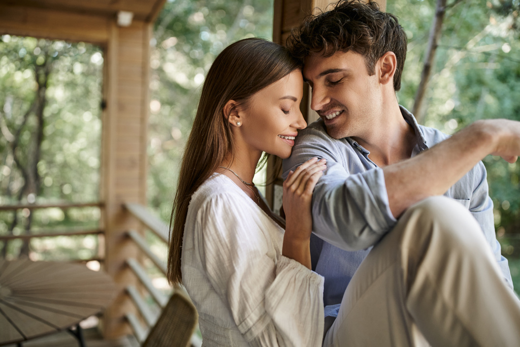 Sorrindo mulher morena em vestido de verão abraçando namorado com olhos fechados perto de casa de férias ao ar livre - Foto, Imagem