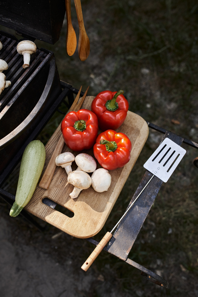 Vista superior de verduras frescas en la tabla de cortar cerca de la barbacoa durante el picnic al aire libre, comida y naturaleza - Foto, imagen