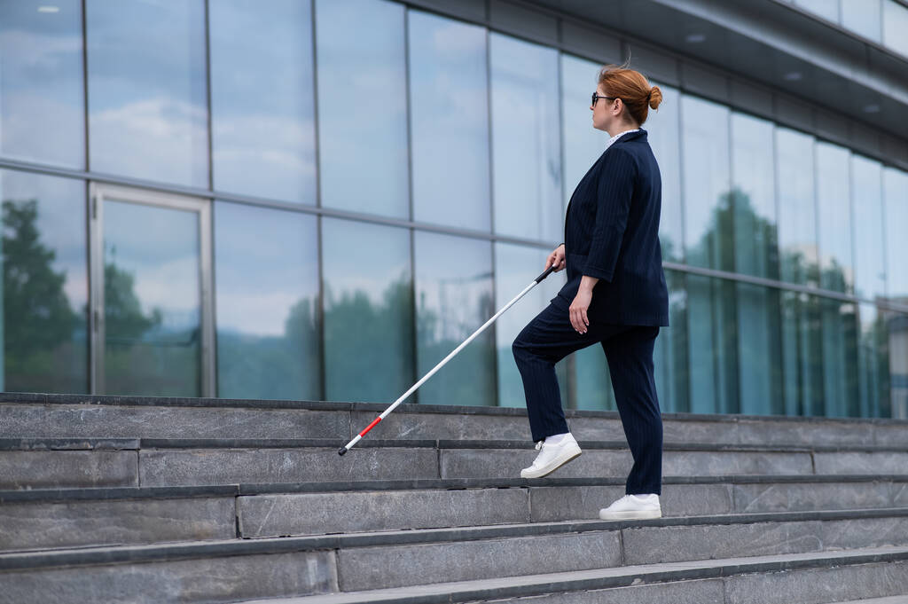 Donna d'affari cieca in occhiali e con un bastone sale le scale per il business center - Foto, immagini