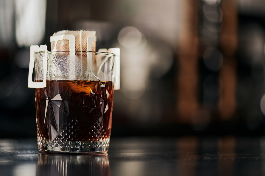 κρυστάλλινο ποτήρι, αλεσμένος καφές σε χάρτινη σακούλα φίλτρου σε μαύρο ξύλινο τραπέζι σε καφέ, μέθοδος στάγδην espresso - Φωτογραφία, εικόνα
