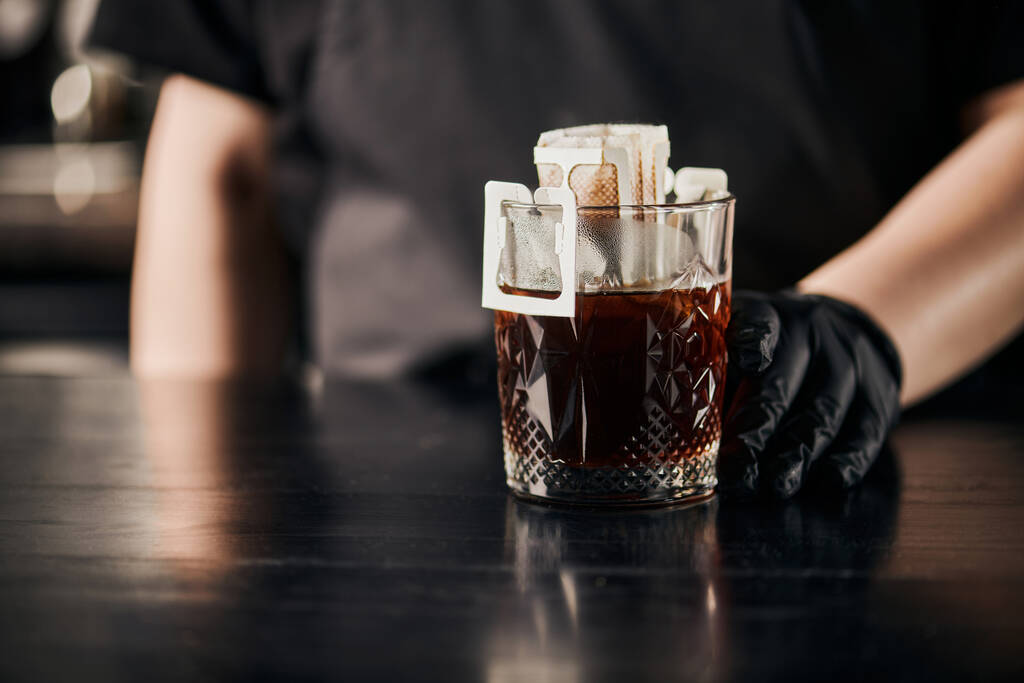 обрезанный вид на пивоварение бариста ароматного кофе в бумажном мешке фильтра и хрустале на черном столе - Фото, изображение