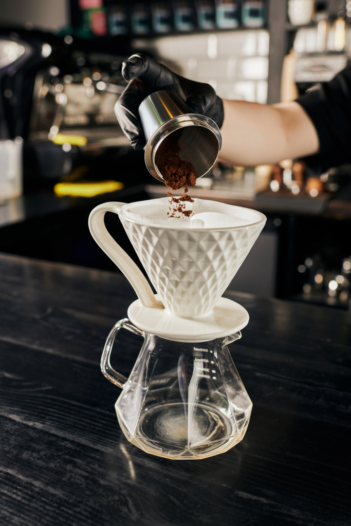 barista toevoegen van fijne gemalen koffie van jigger in keramische druppelaar op glazen pot, V-60 stijl methode - Foto, afbeelding