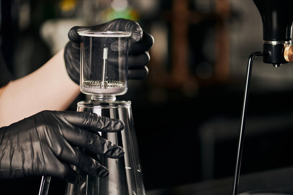 coffee shop, barista in black latex gloves holding siphon coffee maker above glass coffee pot  - Photo, Image