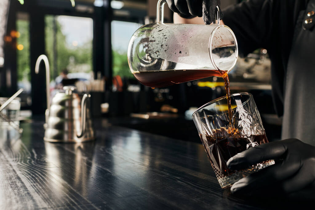 θέα του barista κρατώντας καφετιέρα και χύνοντας πρόσφατα παρασκευασμένο espresso σε κρύσταλλο  - Φωτογραφία, εικόνα