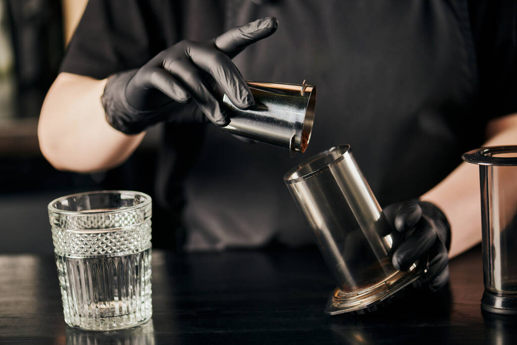 cropped view of barista in black latex gloves pouring ground coffee in aero press near crystal glass - Photo, Image