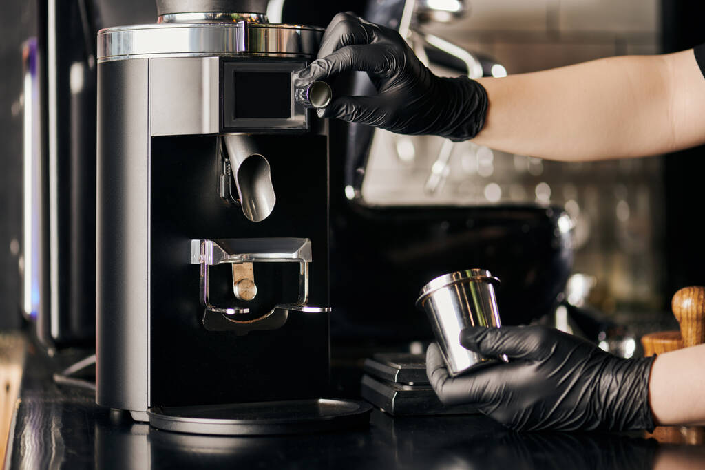 barista em luvas de látex preto operando moedor de café elétrico e segurando copo de medição metálica - Foto, Imagem