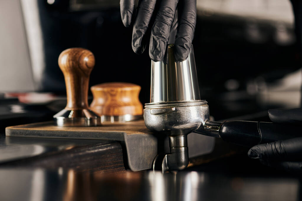 ostříhaný pohled na baristu v černé latexové rukavici lisování kávy v portafiler při přípravě espresso - Fotografie, Obrázek