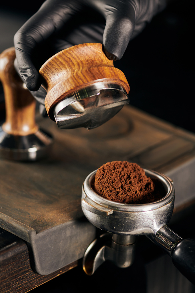 partial view of barista in black latex glove holding tamper near portafilter with ground coffee - Photo, Image