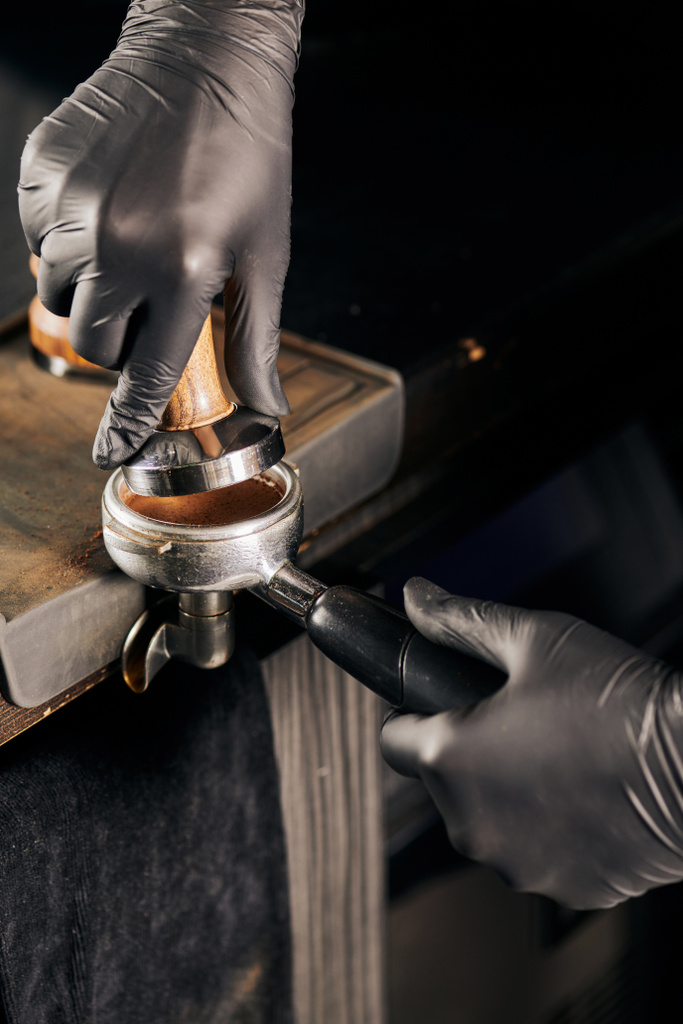 обрізаний вид бариста в чорних латексних рукавичках, що пресують мелену каву в портативному фільтрі - Фото, зображення