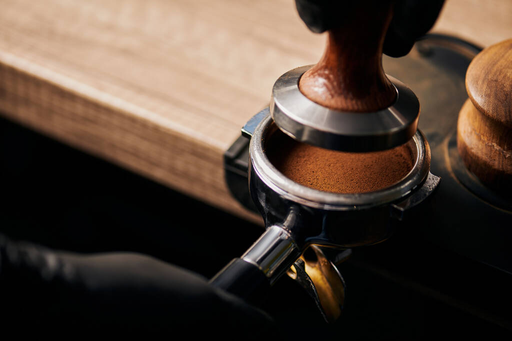 Barista hält Stampfer in der Nähe von Portafilter mit gemahlenem Kaffee, Espresso, Handpresse  - Foto, Bild