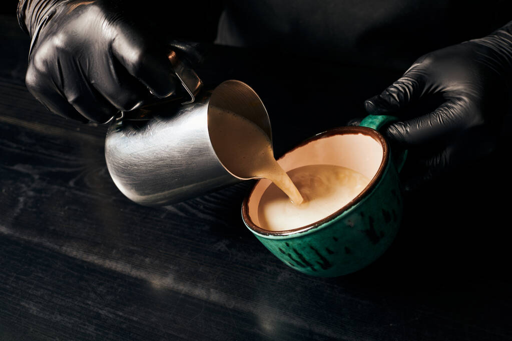 teilweise, Barista in Latexhandschuhen bereitet Cappuccino, Espresso, Latte Art, Krug mit Milch zu  - Foto, Bild