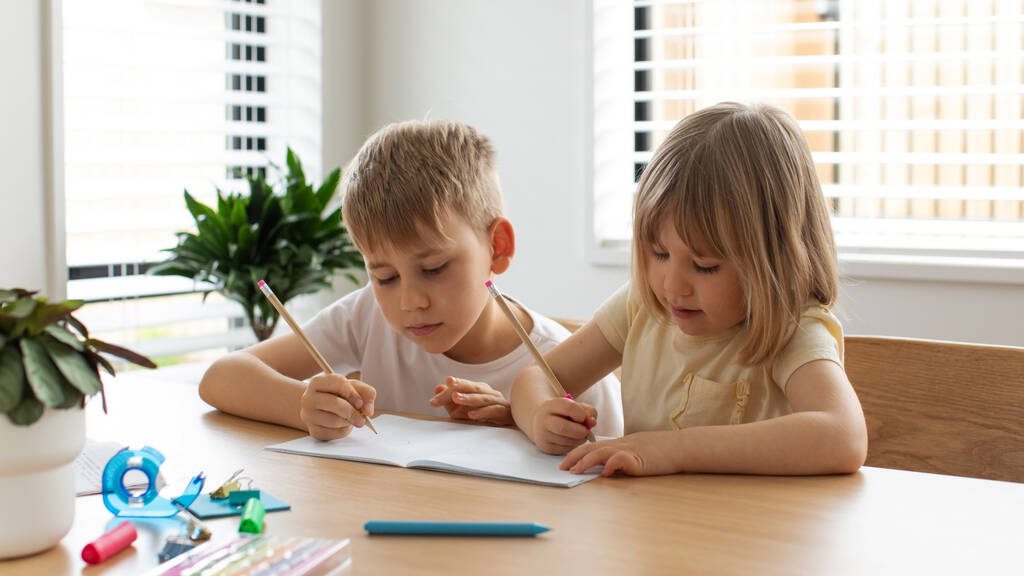 Brother and sister write and draw together with pencils at the table. A friendly family. The concept of home schooling. - Photo, Image