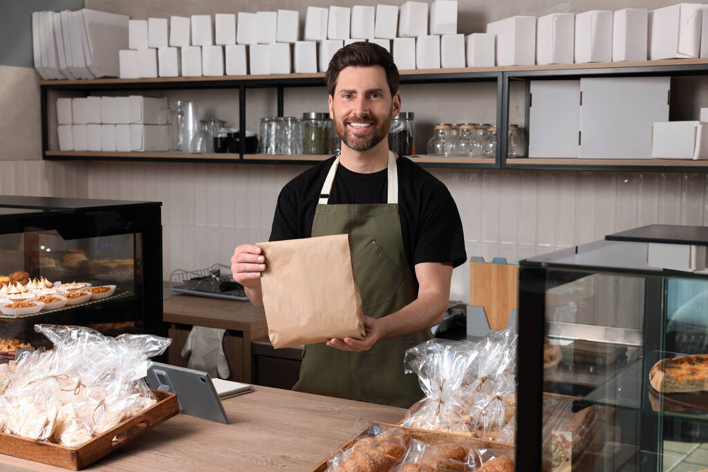 Ευτυχής πωλητής με χάρτινη τσάντα στο ταμείο του αρτοποιείου - Φωτογραφία, εικόνα