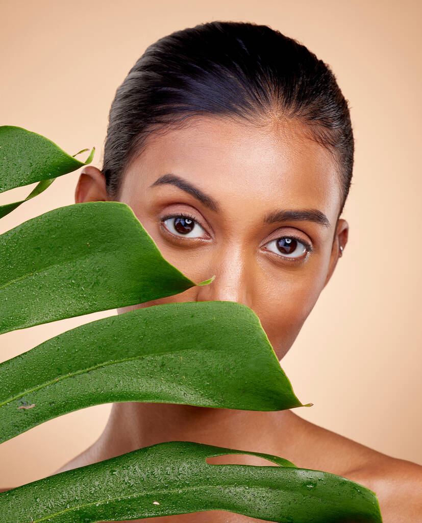 Güzellik, cilt bakımı ve stüdyo arka planında lüks kaplıca bitkisi olan Hintli bir kadınla portre. Dermatoloji, ışıltı ve gülen yüz, yüz bakımı için makyaj malzemesi ve yüz bakımı için yapraklar. - Fotoğraf, Görsel