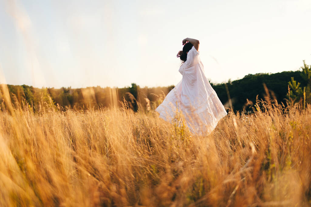 Brunette young woman in wild field. Natural beauty and romance concept. Sunset light. View from the back. - Photo, Image