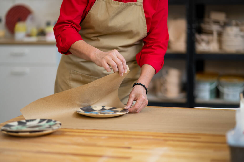 Руки женщины-гончара мастер упаковки глиняных изделий по заказу клиента на бумагу на рабочем месте - Фото, изображение