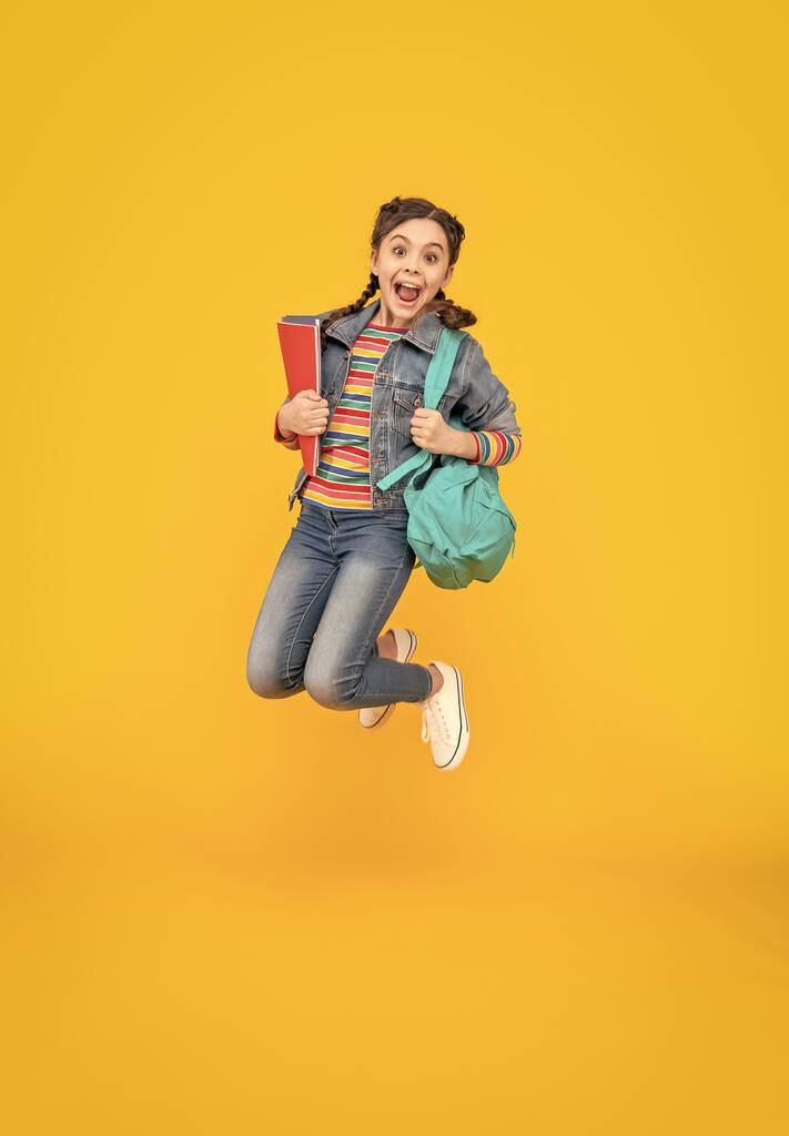 Excited schoolgirl screaming in midair, school. Energetic girl jumping after school yellow background. Back to school. - Photo, Image