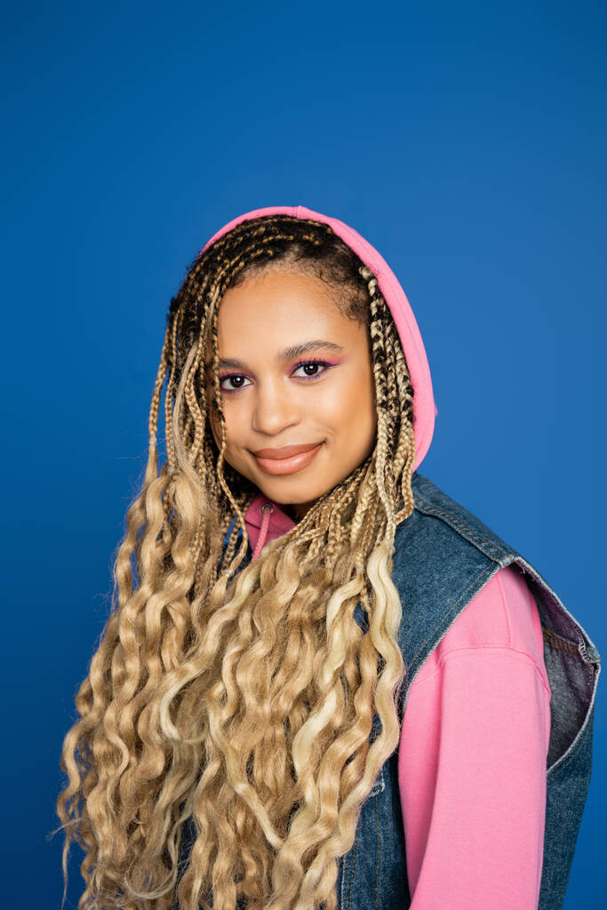 portrait of african american woman in pink hood smiling and looking at camera, blue background - Photo, Image