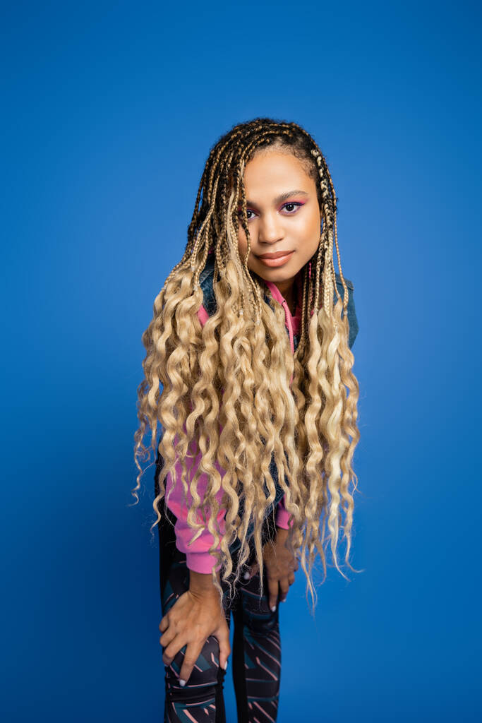 beautiful african american woman with dreadlocks and bold makeup looking at camera on blue - Photo, Image
