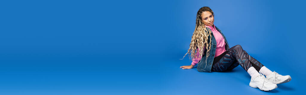 comprimento total de cabelos longos mulher americana africana em roupas esportivas sentado em azul, banner - Foto, Imagem