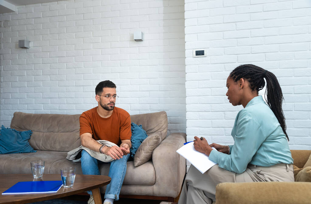 Young depressed man crying talking to mental health counselor during a session in the office. Stressed male at psychotherapy after divorce having emotional damage issue. Relationship difficulties. - Photo, Image
