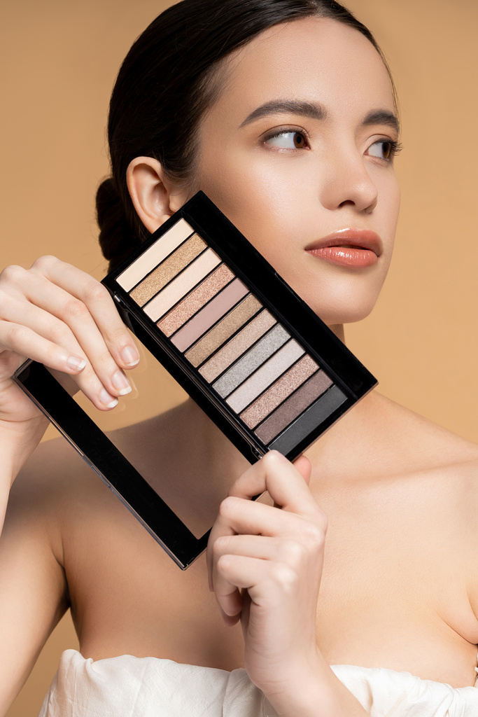 Asiatisches Model mit perfekter Haut hält Lidschatten-Make-up-Palette und posiert isoliert auf Beige - Foto, Bild
