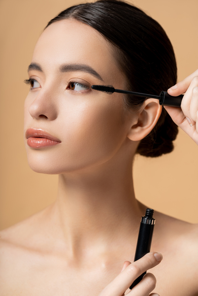 Jeune femme asiatique avec maquillage naturel tenant mascara et applicateur isolé sur beige - Photo, image