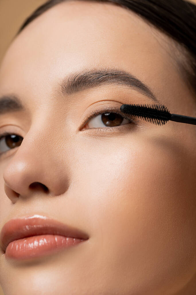 Close up view of asian woman with natural visage posing near mascara applicator isolated on beige - Photo, Image