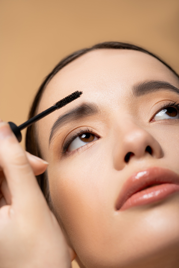 ベージュで隔離された眉毛ゲルを適用する自然な構造を持つ若いアジアの女性のクロップビュー - 写真・画像