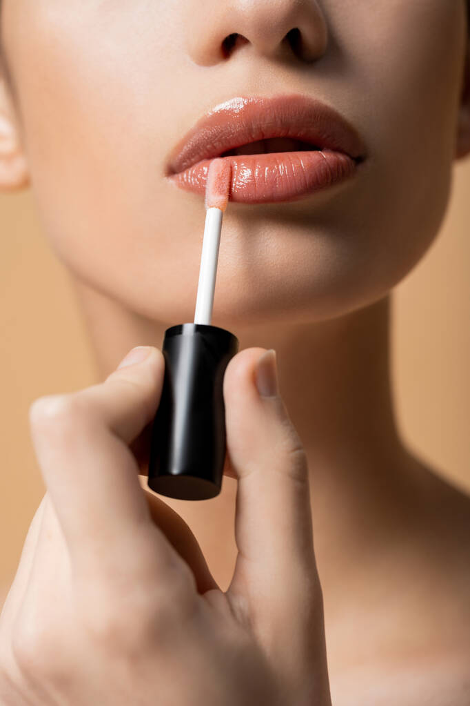 Gewassen weergave van jonge vrouw het aanbrengen van lipgloss terwijl het doen van make-up geïsoleerd op beige - Foto, afbeelding