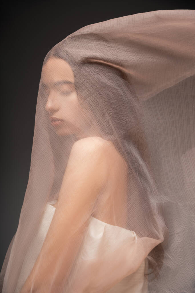 Портрет красивої азіатської моделі з закритими очима позує під бежевою тканиною ізольовано на чорному - Фото, зображення