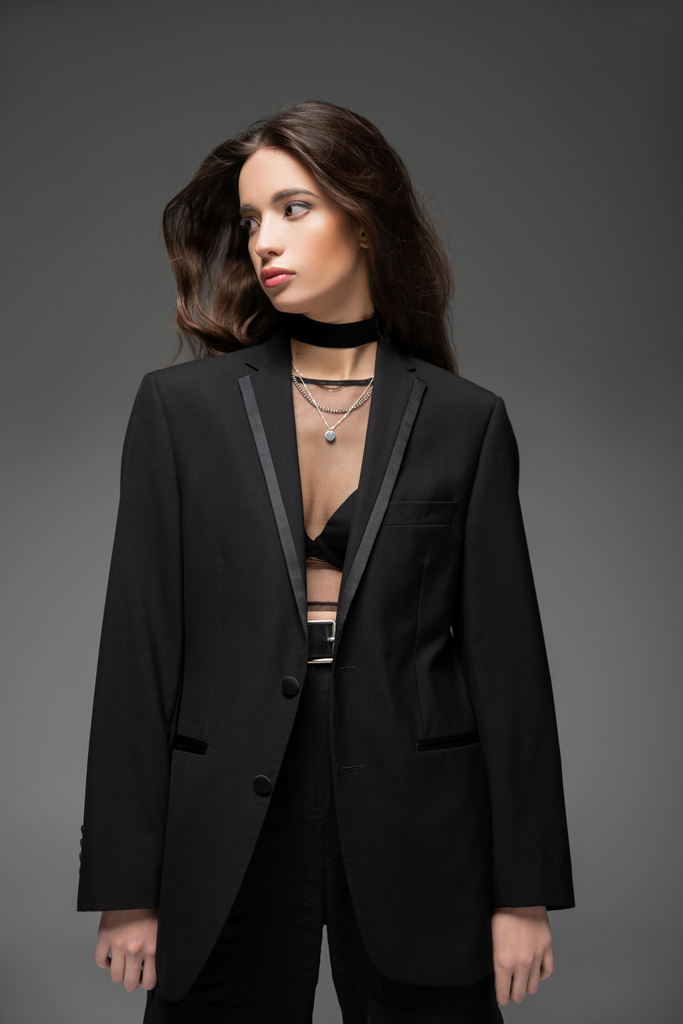 Trendi ázsiai modell hálós felső és fekete kabát néz félre, miközben pózol elszigetelt szürke - Fotó, kép