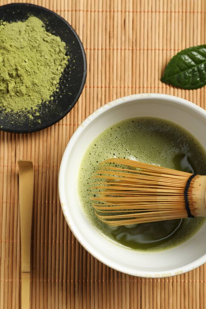 Tasse frischen Matcha-Tee mit Schneebesen, Löffel und grünem Pulver auf Bambusmatte, flach gelegt - Foto, Bild