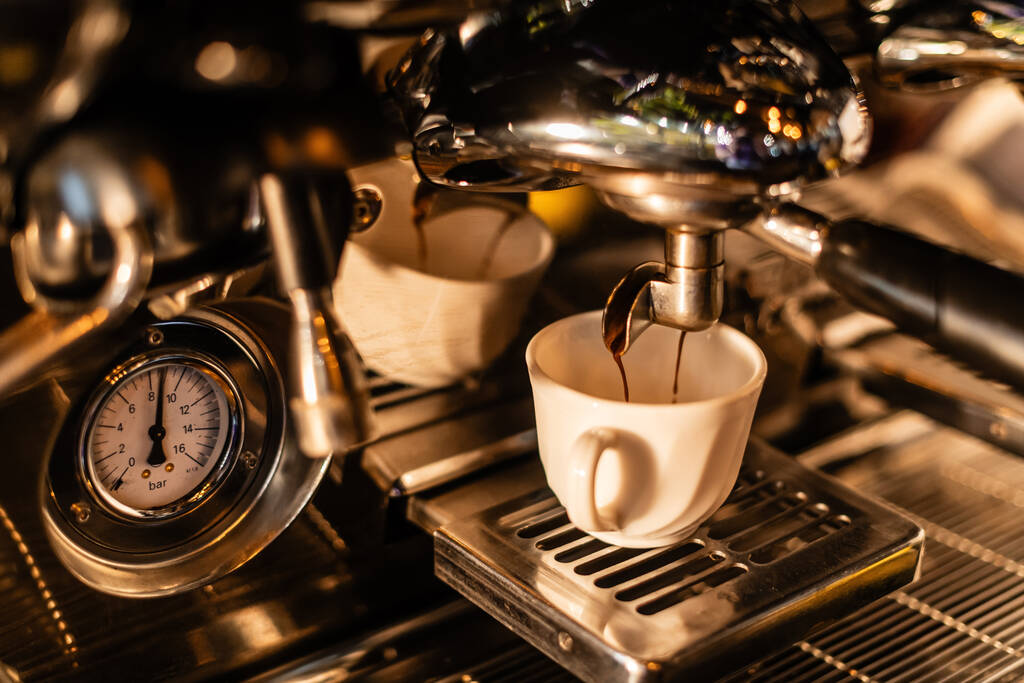 カフェで日光を浴びたホワイトカップのマシンから注ぐコーヒーのビューを閉じる - 写真・画像