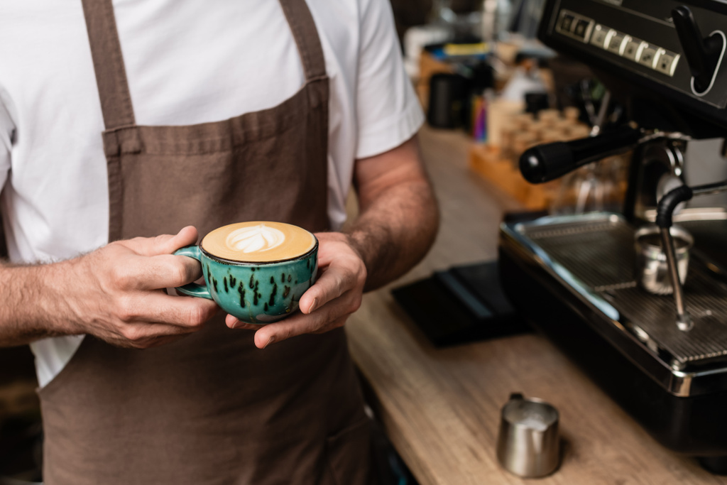 zugeschnittene Ansicht von Barista in Schürze mit Cappuccino-Tasse während der Arbeit im Café - Foto, Bild