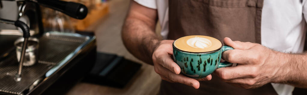 обрезанный вид на бариста в фартуке с чашкой капучино в кофейне, баннер - Фото, изображение