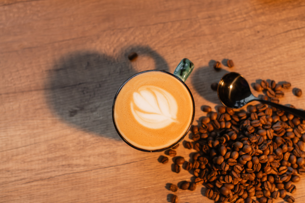 top view csésze cappuccino közel kávébab és kanál a munkaasztalon kávézóban - Fotó, kép