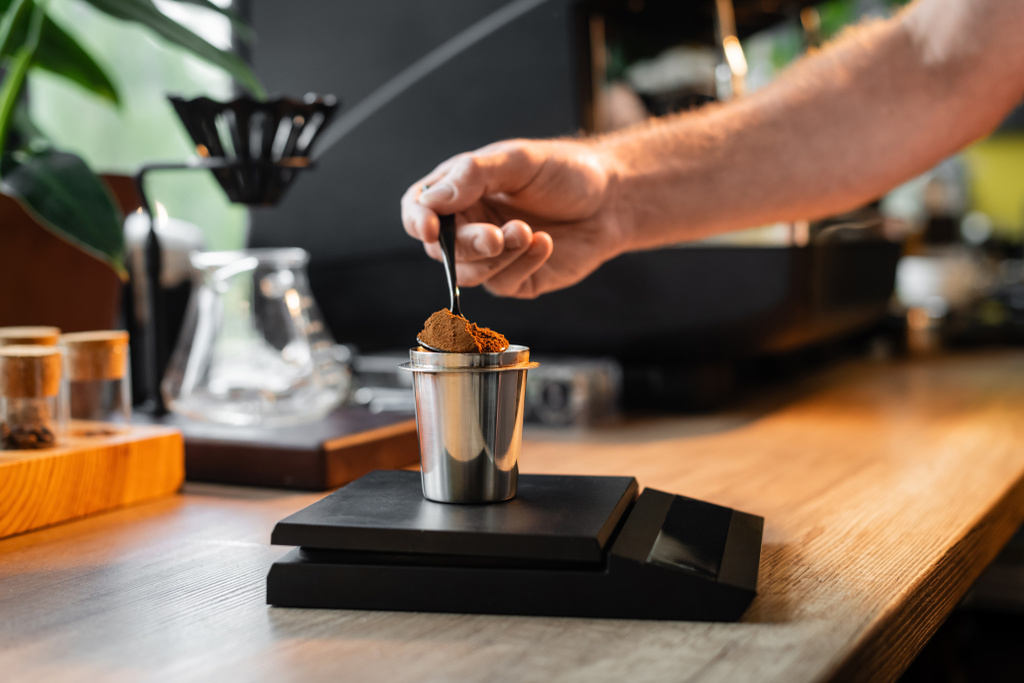 bijgesneden weergave van barista gieten van koffie in beker op elektronische weegschalen in de buurt van koffiezetapparaat in cafe - Foto, afbeelding