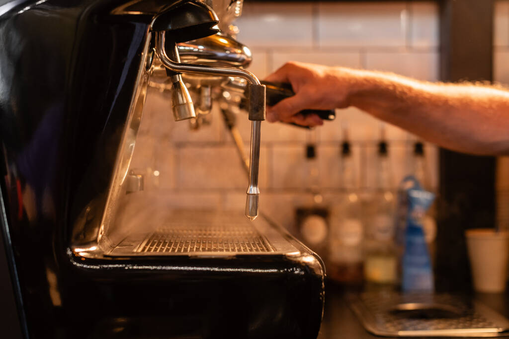 καλλιεργημένη άποψη θολή barista χρησιμοποιώντας μηχανή καφέ κοντά στον ατμό και το φωτισμό στην καφετέρια - Φωτογραφία, εικόνα
