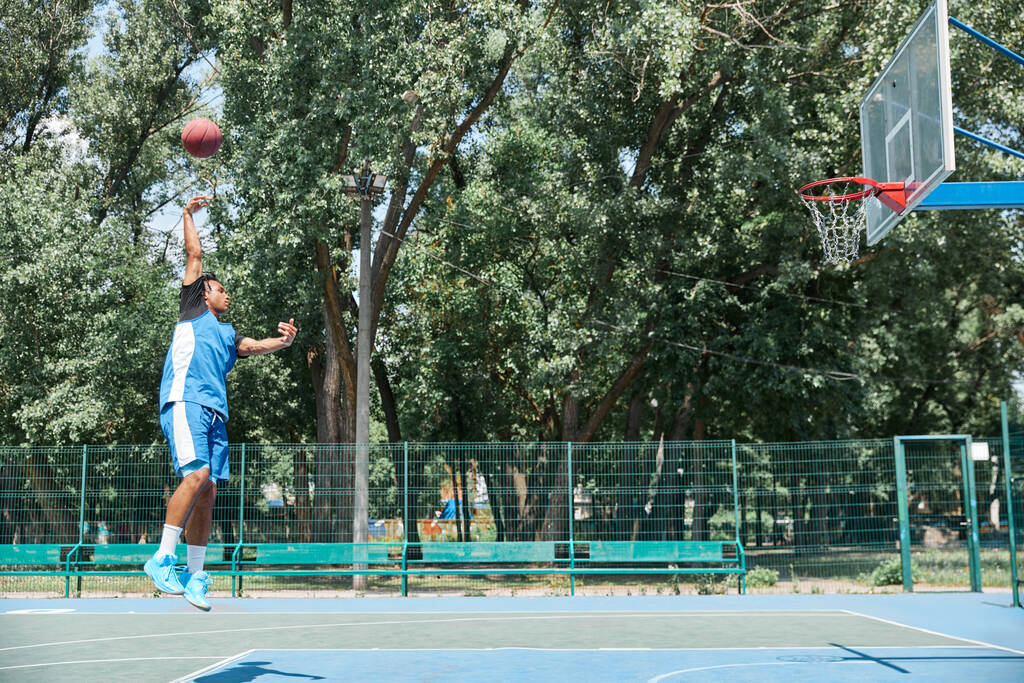 Mladý sportovec, sportovec v modrém unifroman tréninku, hraje basketbal venku na sportovním hřišti za teplého slunečného dne. Koncept profesionálního sportu, soutěže, hobby, hry, aktivního životního stylu - Fotografie, Obrázek