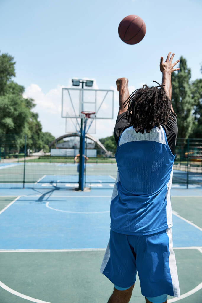 Jeune homme concentré, athlète en uniforme bleu jouant au basket, jetant la balle dans le panier. Formation en plein air. Concept de sport professionnel, compétition, passe-temps, jeu, mode de vie actif - Photo, image