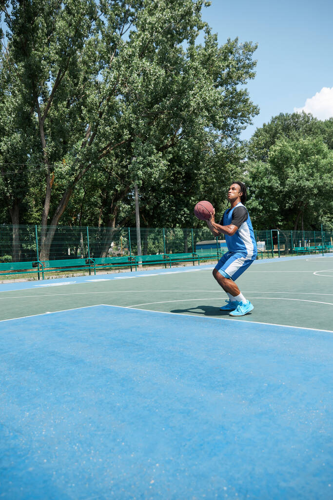 Jongeman, atleet in blauw uniform training, basketbal spelen buiten op warme zomerdag. Begrip professionele sport, competitie, hobby, spel, actieve levensstijl - Foto, afbeelding