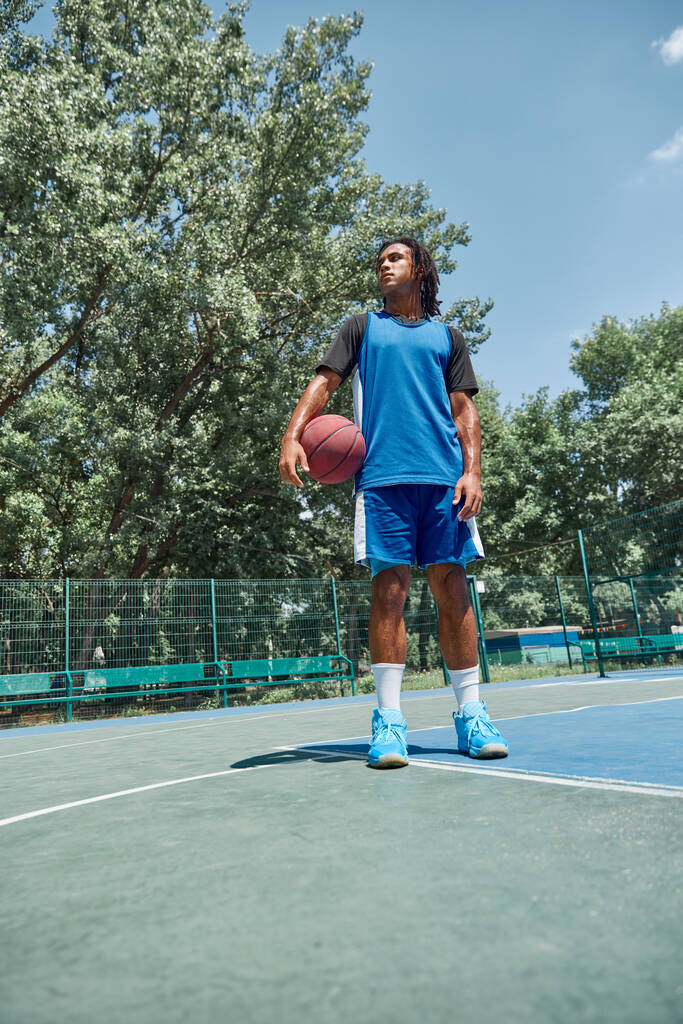 Mavi üniformalı, dışarıda basketbol topuyla poz veren genç bir adamın portresi. Profesyonel spor, rekabet, hobi, oyun, aktif yaşam tarzı kavramı - Fotoğraf, Görsel