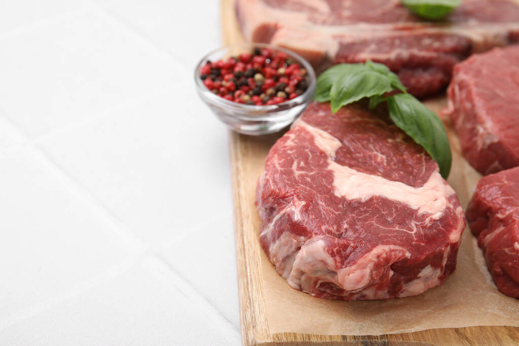 Cut fresh beef meat, spices and basil leaves on white tiled table, closeup. Space for text - Foto, imagen