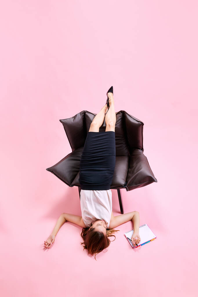 Geschäftsfrau ungemütlich auf Sessel liegend, arbeitend, Notizen vor rosa Studiohintergrund machend. Geschäftskonzept, Arbeitsroutine, Fristen, Freiberuflichkeit, Büro, Anzeige - Foto, Bild