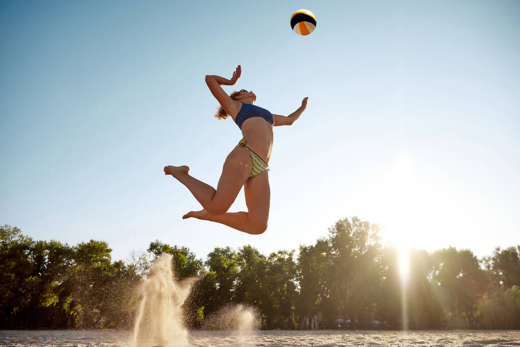 Plaj voleybolu oynayan genç bir kadının dinamik alttaki görüntüsü. Arka planda zıplayarak topa vuruyor. Spor anlayışı, aktif ve sağlıklı yaşam tarzı, hobi, yaz zamanı, reklam - Fotoğraf, Görsel